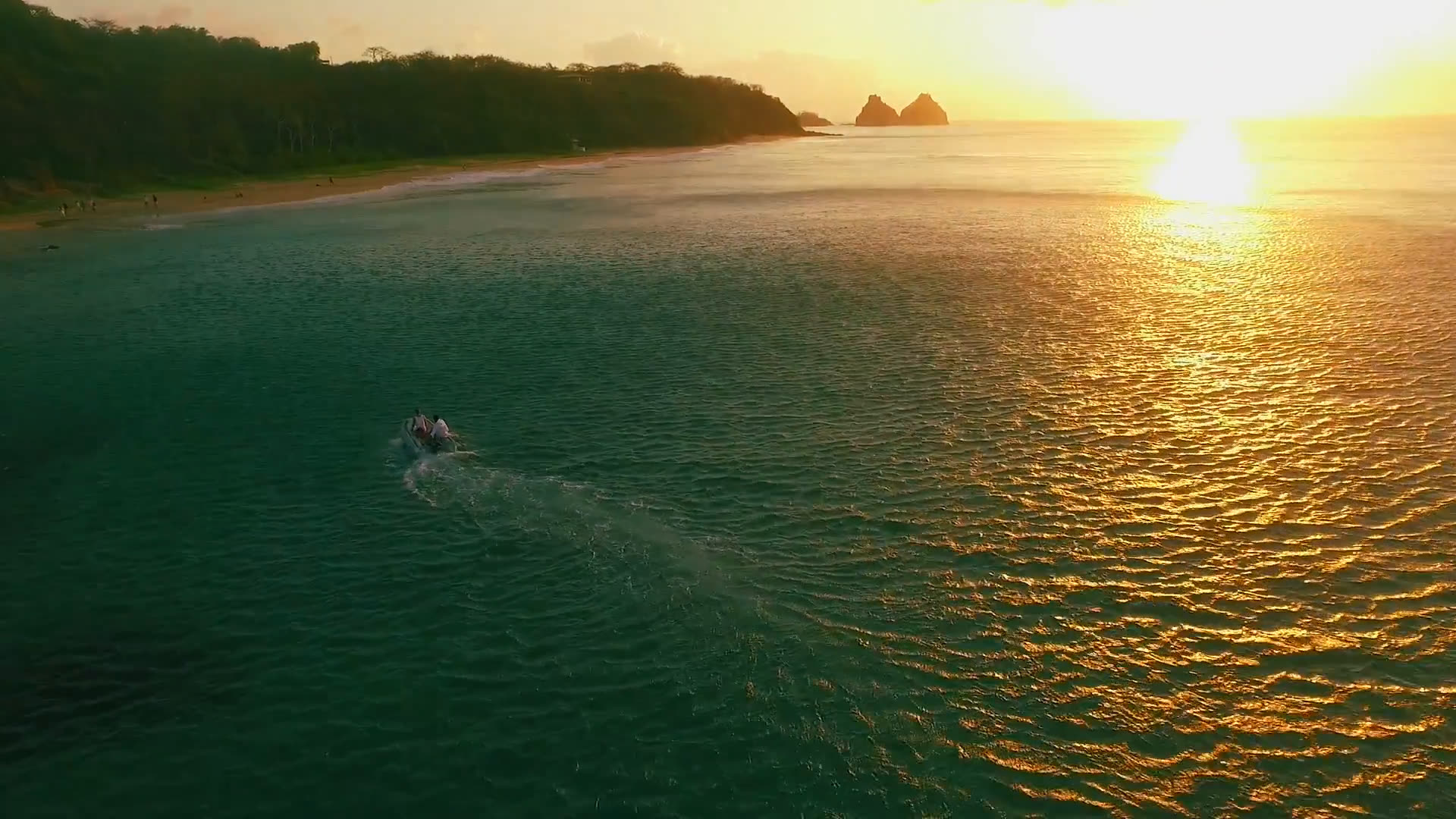 Veleiro navegando em águas douradas ao pôr do sol diante da costa de Fernando de Noronha