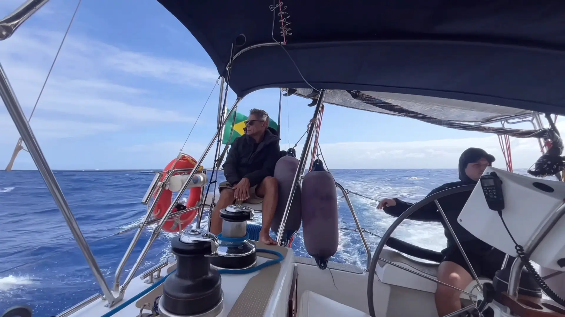 Cockpit de veleiro com a tripulação e a bandeira do Brasil na popa
